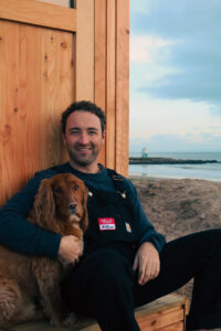 Will, founder of Hikitalo, sitting outside the sauna with his dog, Archie.