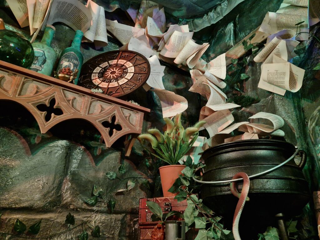 Ruffled book pages, dusty glass bottles, a cauldron and other items adorn the corner of a room