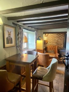 An image of The Cross Keys bar area, showing wooden bar tables and chairs, and leather armchairs.
