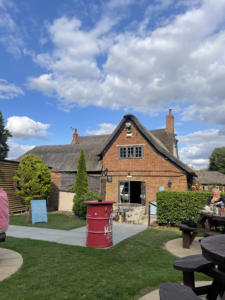 Image of the back of The Cross Keys pub and garden area, with people sat at wooden picnic tables.